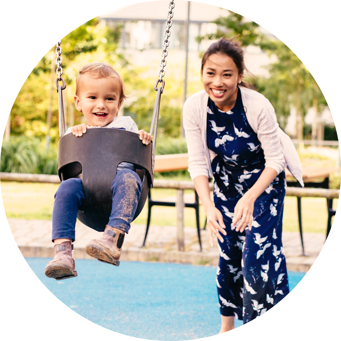 Happy mother pushes laughing child on swing